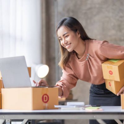 SME Online seller Young Asian woman working on laptop and box checking online order, check goods stock delivery package shipping postal. Asian woman startup SME small business at home office